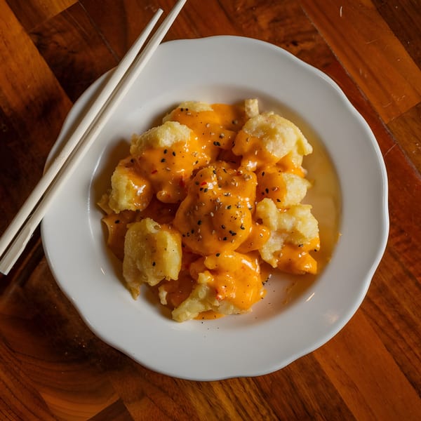 Crispy fried shrimp coated in a vibrant orange sauce, topped with sesame seeds, served with chopsticks.