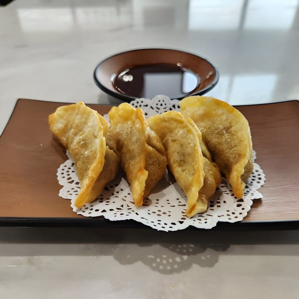 Golden-fried dumplings on a brown plate with a white doily, served with a side of soy sauce.