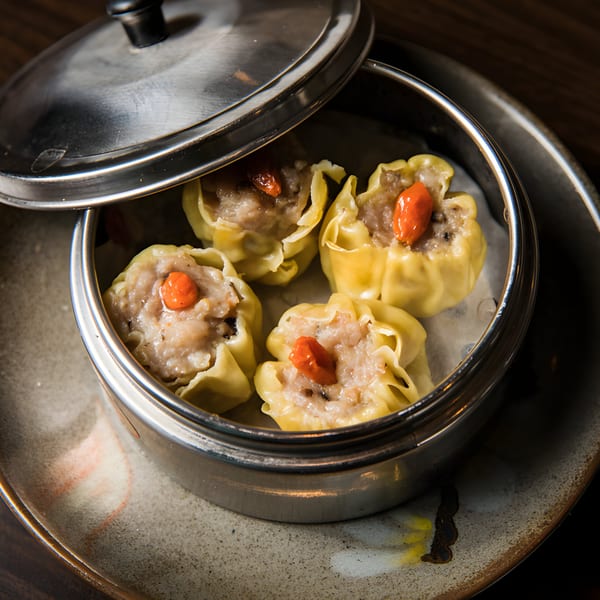Four steamed pork and shrimp shumai dumplings with goji berries in a metal steamer.
